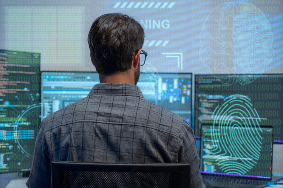 Man at a computer with 3 monitors displaying programming code